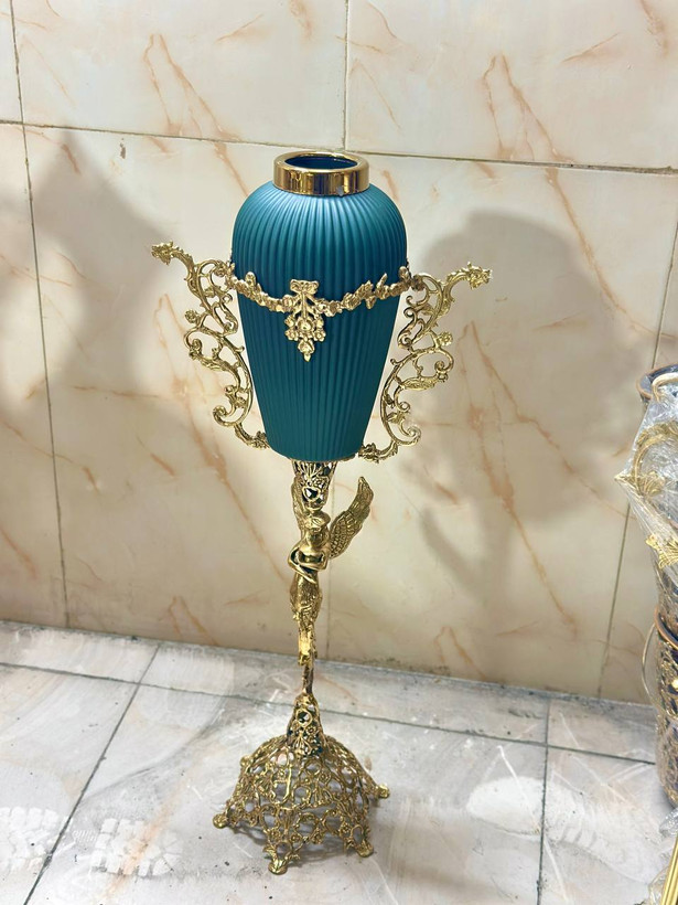 گلدان کنار سالنی تمام برنجی بزرگ با پایه توری مشبک، دستههای تندیسی فرشته بالدار، بدنه نقش برجسته گل ارکیده و روکش نانو کوره در سه رنگ بازرگانی نداف مشهد