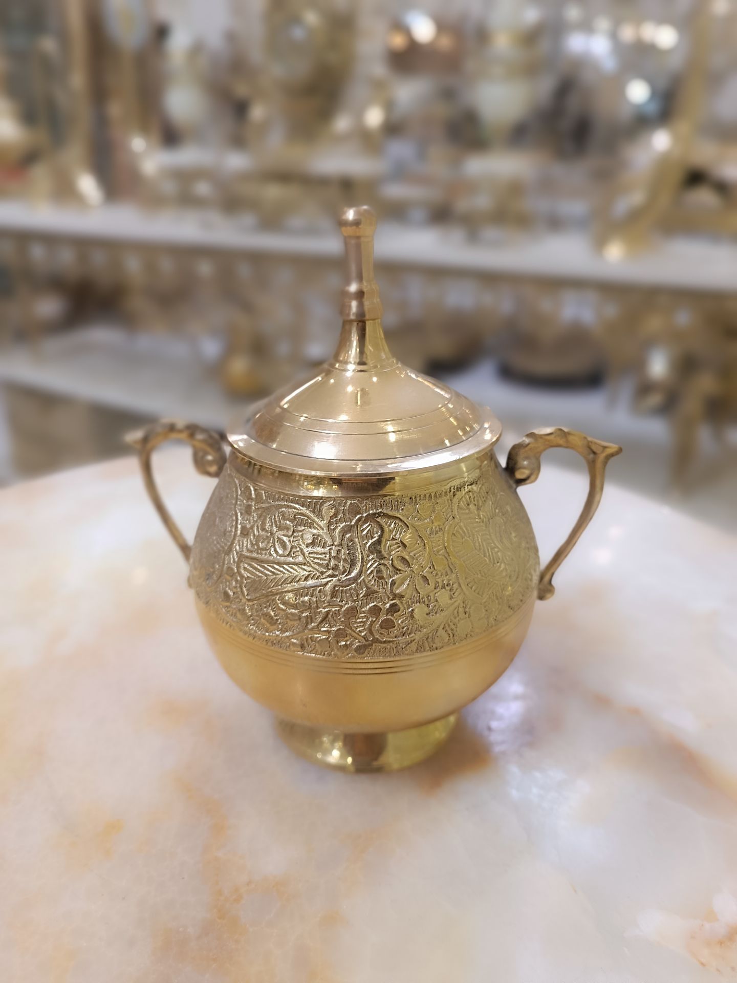 قندان تمام برنجی طلایی دارای درب و دو دسته با حکاکی‌های برجسته طرح پرنده و گل روی پس‌زمینه محو فروشگاه متالوکس